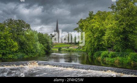 Cascades d'eau et petite chute d'eau sur la rivière Suir entourée d'une forêt verdoyante et de l'église St Paul en arrière-plan, Cahir, Irlande Banque D'Images