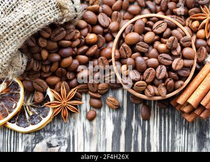 Les grains de café sont versés d'une toile à chandelier dans une tasse en bois, sur une table en bois il y a des bâtons de cannelle, des quartiers de citron séchés et anis, vue de dessus. Banque D'Images