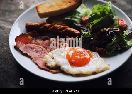 Petit déjeuner anglais frit œufs, jambon, saucisse, bacon, salade et toasts sur fond de bois dans la lumière mystique Banque D'Images