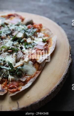 Pizza avec tomates au jambon, fromage mozzarella et basilic. Délicieuse pizza italienne sur un plateau de pizza en bois, dans une lumière mystique Banque D'Images