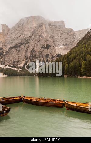 Des bateaux en bois amarrés dans un lac calme et vert entouré par Rochers majestueux et collines boisées dans la chaîne de montagnes des Dolomites Italie Banque D'Images