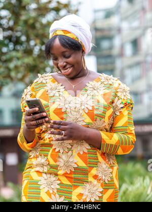 De dessous de femme noire souriante dans la navigation de vêtements ornementaux sur un téléphone portable en ville Banque D'Images