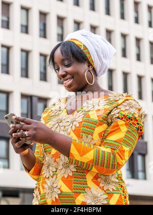 De dessous de femme noire souriante dans la navigation de vêtements ornementaux sur un téléphone portable en ville Banque D'Images