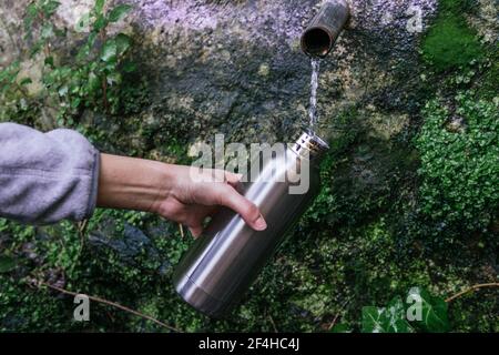 Crop anonyme randonneur remplissant la bouteille en métal avec frais froid naturel source d'eau de source avec pipe dans la forêt montagneuse Banque D'Images