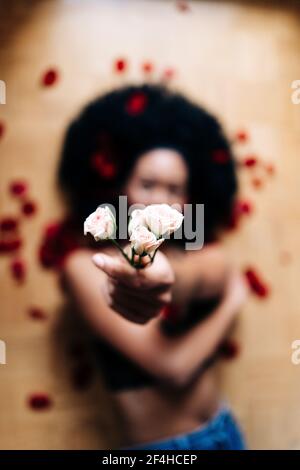 Par-dessus une femme afro-américaine anonyme située sur le sol avec des pétales épars et des fleurs de rose tendres à l'appareil photo Banque D'Images