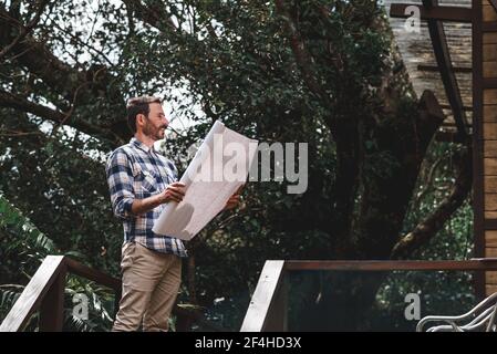 Vue latérale à angle bas d'un architecte mâle avec tirage de papier terrasse de maison en bois en forêt Banque D'Images