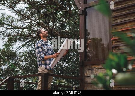 Vue latérale à angle bas d'un architecte mâle avec tirage de papier terrasse de maison en bois en forêt Banque D'Images