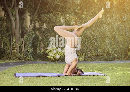 Vue latérale de la femme flexible heureuse dans les vêtements de sport de démonstration Adho Mukha Vrkssasana pose avec les jambes fléchis tout en pratiquant le yoga sur le tapis et en regardant un Banque D'Images