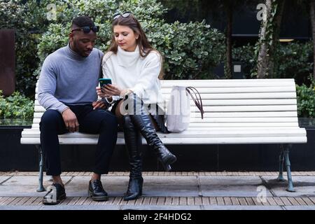Contenu couple multiracial adulte amoureux écouter de la musique sur mobile téléphone tout en passant du temps ensemble dans le parc Banque D'Images