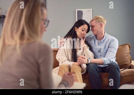 Contenu couple multiracial assis sur un canapé dans le bureau du psychologue et s'embrasser pendant le rendez-vous de psychothérapie Banque D'Images