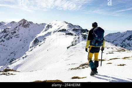 Vue arrière d'un grimpeur méconnu qui marche sur une pente de neige chaîne de montagnes rocheuses couverte par temps ensoleillé Banque D'Images