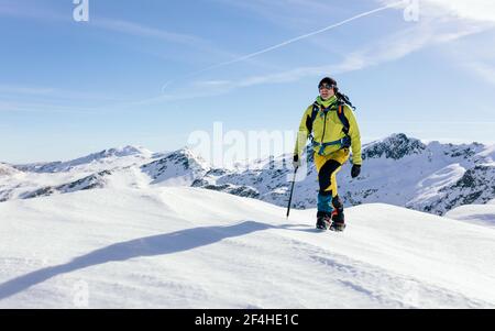 Grimpeur mâle dans l'extérieur marchant sur une pente de neige couverte chaîne de montagnes rocheuses par temps ensoleillé Banque D'Images