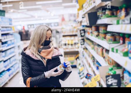 Femme dans un masque protectivel et des gants en caoutchouc se tient dans un supermarché et des produits d'horlogerie. Banque D'Images