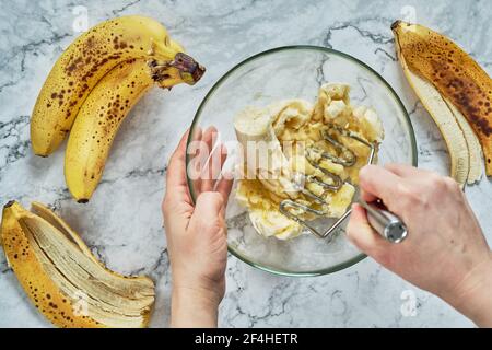 Femme à la main écrasant plusieurs bananes pour cuire dans un pain de banane. Banque D'Images