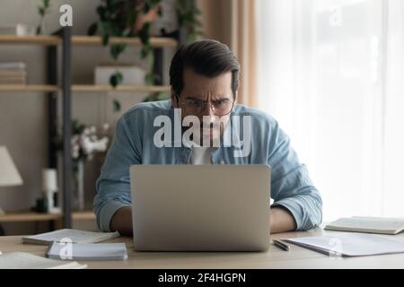 Gros plan homme d'affaires perplexe portant des lunettes regardant l'écran d'un ordinateur portable Banque D'Images