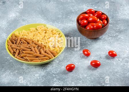 Deux sortes de pâtes crues sur l'assiette avec un bol de tomates Banque D'Images