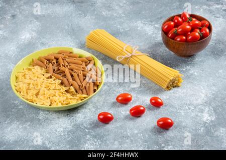 Deux sortes de pâtes crues sur plaque avec tomates et spaghetti Banque D'Images