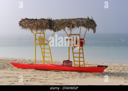 Tours de sauvetage jaunes vides avec toit en chaume de palmier et lumineux faites du kayak rouge par une journée de brouillard sur une plage déserte Banque D'Images