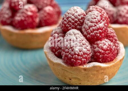 Ensemble de tartelettes de framboises appétissantes avec sucre glace sur une base éponge spongieuse sur une table en bois. Banque D'Images