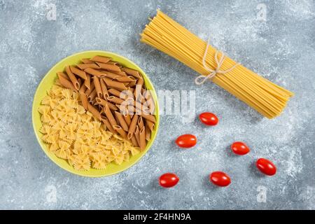 Deux types de pâtes crues sur plaque avec tomates et spaghetti Banque D'Images