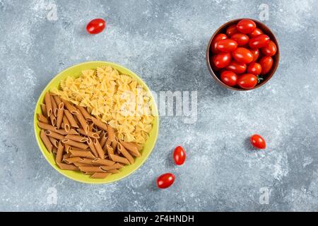 Deux sortes de pâtes crues sur l'assiette avec un bol de tomates Banque D'Images