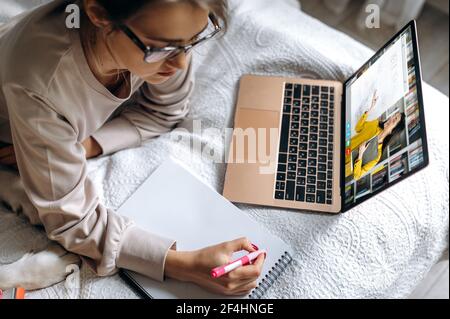 Cours en ligne pendant l'apprentissage à distance, à l'écran, une enseignante explique le sujet de la leçon. Une fille utilise un ordinateur portable, écoute une conférence en ligne, prend des notes, étudie à la maison, appelle vidéo Banque D'Images