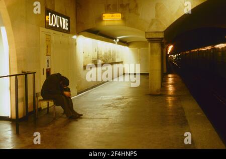 Tramp de couchage assis sur le banc au bout de la plate-forme à la station de métro du Louvre, Paris, France, fin des années 70. Banque D'Images