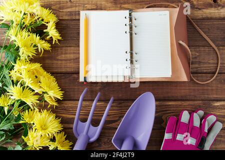 pose à plat avec bloc-notes, outils de jardinage, gants et chrysanthèmes sur une table en bois. Banque D'Images