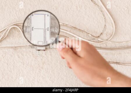 La main d'un travailleur inspecte un grand répartiteur d'antenne avec une loupe, gros plan. Banque D'Images