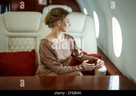 une jolie femme blonde habillée dans une élégante robe beige est présente dans un siège confortable sur un jet privé Banque D'Images