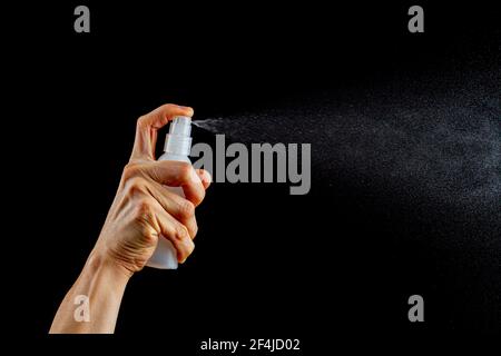 Une femme caucasienne tient une petite bouteille de pulvérisation fine en plastique et appuie sur le bouton supérieur pour vaporiser un liquide incolore. Image polyvalente Banque D'Images