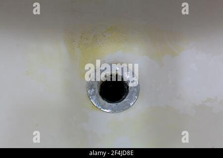 Vue rapprochée d'un gouffre ou d'un trou de baignoire dans une salle de bains sale. Il y a des décolorations jaunes et sombres visibles et des restes de calcaire et de savon accumulat Banque D'Images