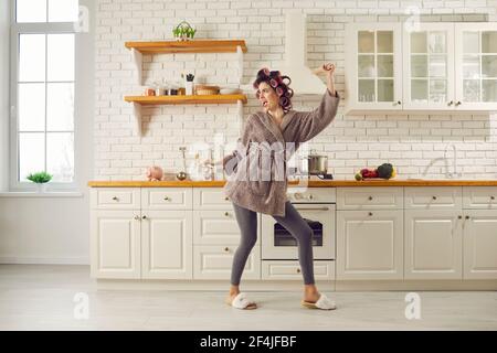 Drôle femme de ménage chantant et dansant tout en cuisinant le dîner dans elle cuisine spacieuse Banque D'Images