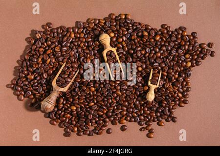 Grains de café torréfiés sur fond marron. Vue de dessus. Grains de café dans une cuillère en bois. Banque D'Images