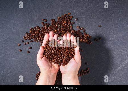 Grains de café bruns grillés sur fond gris. Modèle pour la publicité du café en forme coeur dans la main. Vue de dessus. Banque D'Images