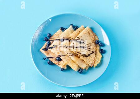 Crêpes faites maison, crêpes fines savoureuses avec chocolat et baies sur une assiette bleue pour le petit déjeuner avec une tasse de thé. Cuisine russe traditionnelle. Banque D'Images
