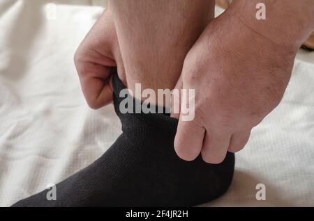 Les mains d'un homme adulte mettent de nouvelles chaussettes. Un homme à la maison le matin met des chaussettes grises sur sa jambe. Cliquez. Mise au point sélective Banque D'Images