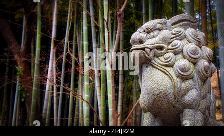 L'une des nombreuses statues de lion ornementées que l'on trouve à Kamakura, au Japon, en face d'une forêt de bambous. Banque D'Images