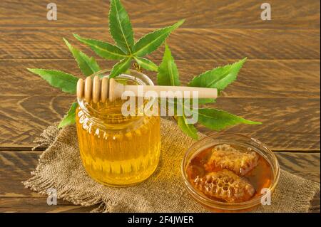 pot en verre de miel, balancier en bois et feuilles de chanvre gros plan sur fond en bois. CBD produits sains. Dessert sucré. Médecine alternative. Banque D'Images