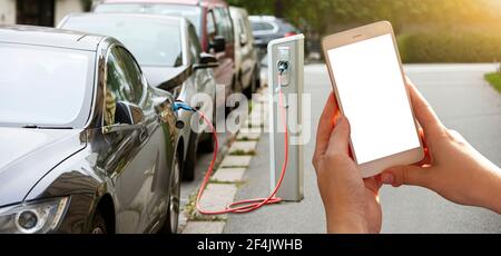 Mains avec un smartphone sur un fond de voiture de location à la station de charge pour les véhicules électriques. Partage de voiture. Banque D'Images