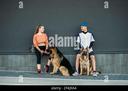 Amour des animaux, entraînement des chiens, meilleures races de chiens pour la famille. Jeunes couples sportifs marchant avec deux chiens de berger allemands en plein air dans le parc d'été Banque D'Images