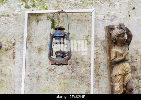 le mur du jardin abandonné. lampe au kérosène et statue en bois pour enfant qui y est accrochée. Banque D'Images