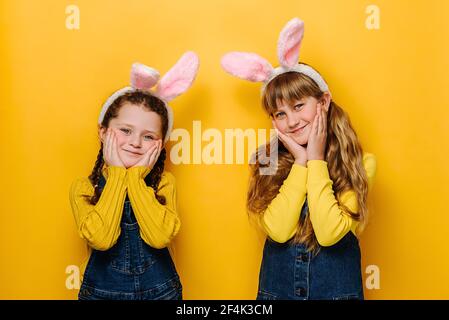 Charmantes petites filles charmantes garde les mains sur les joues, belles sœurs avec l'expression amicale, vêtues d'oreilles moelleuses de lapin rose Banque D'Images