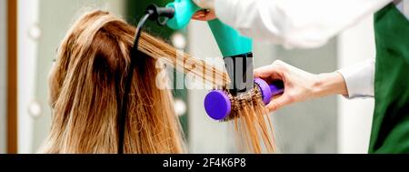 Vue arrière de la jeune femme recevant des cheveux de séchage avec un sèche-cheveux et brosse à cheveux dans un salon de coiffure Banque D'Images