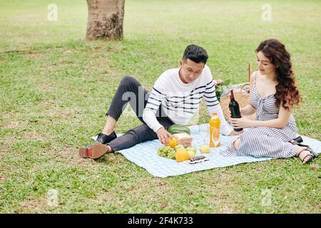 Jeune couple vietnamien assis sur une couverture dans le parc et de prendre le vin et la nourriture sont sortis du panier Banque D'Images