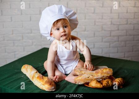 Petit garçon dans un chapeau et avec du pain. Petit enfant habillé comme un cuisinier dans la cuisine. Banque D'Images