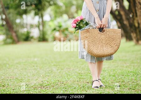 Image rognée de jeune femme debout dans le parc avec du rose roses dans son sac en osier Banque D'Images