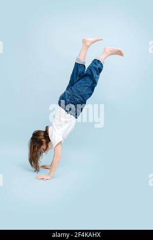 Petite fille debout sur ses mains pendant un moment, elle est en transition. Sur fond bleu. Prise de vue en studio. Banque D'Images