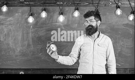 Le professeur de lunettes tient le réveil. Concept de calendrier et de régime. Homme avec barbe et moustache sur le visage confus dans la salle de classe. Boxer taille basse à barbe Banque D'Images