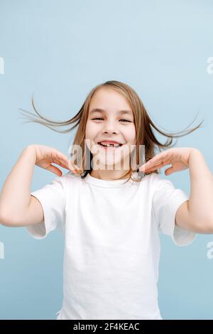 Femme de 9 ans souriante et édentée sur fond bleu. Prise de vue en studio. Elle porte un Jean bleu et une chemise blanche. Elle joue avec son épaule mince-l Banque D'Images